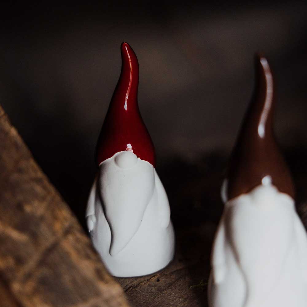 Ein Paar Zwergenfiguren aus Keramik von Storefactory Svante Wichtel Keramik mit roten und braunen Hüten stehen auf einer Holzoberfläche.