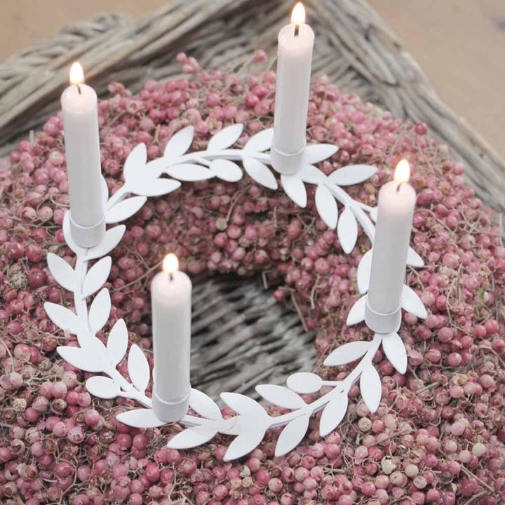 Ein dekorativer Kranz, geschmückt mit rosa Beeren, kombiniert mit einem weißen Kerzenhalter mit Blättern von VL Home, der vier leuchtend weiße Kerzen präsentiert.