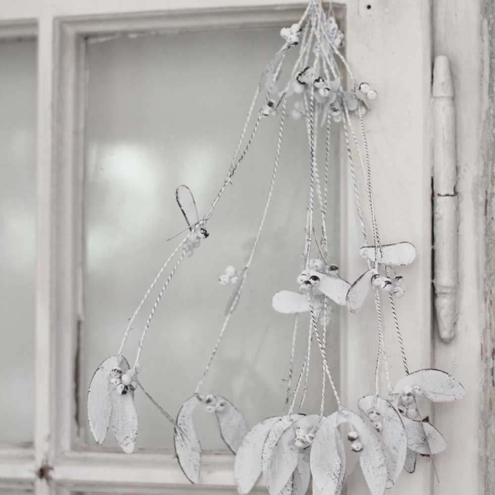 Ein VL Home - Mispel Metall Shabby Chic Hänger mit 38 cm Durchmesser und weißem Deko-Design mit Blättern und Beeren hängt an einem alten, rustikalen Fenster.