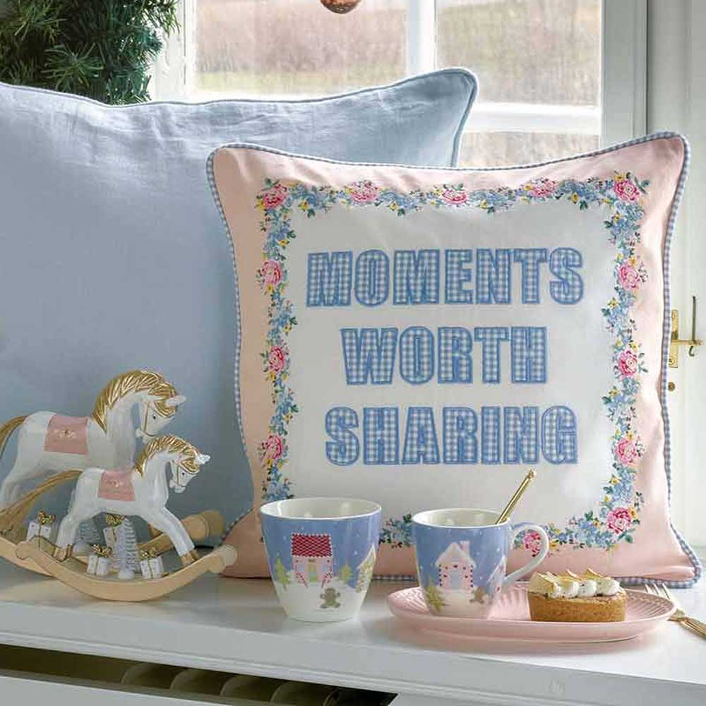 Dekoratives Kissen mit der Stickerei „Moments Worth Sharing“, daneben ein hölzernes Schaukelpferd und zwei Tassen Tee mit Scones auf einem Tablett und die GreenGate - Alice Servierplatte.