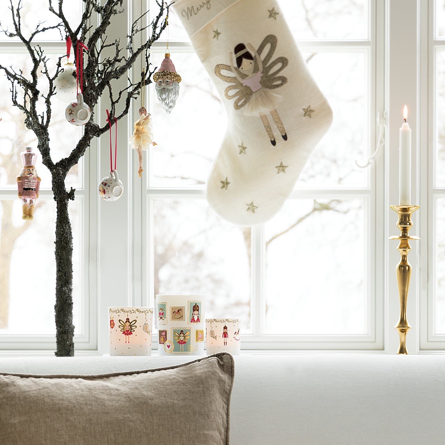 Eine festliche Szene zeigt ein GreenGate Weihnachtsbuchstaben-Aufkleberset in Weiß auf einem Fenster, mit Kerzen, Ornamenten und dekorativen Haltern, die das Fensterbrett schmücken.