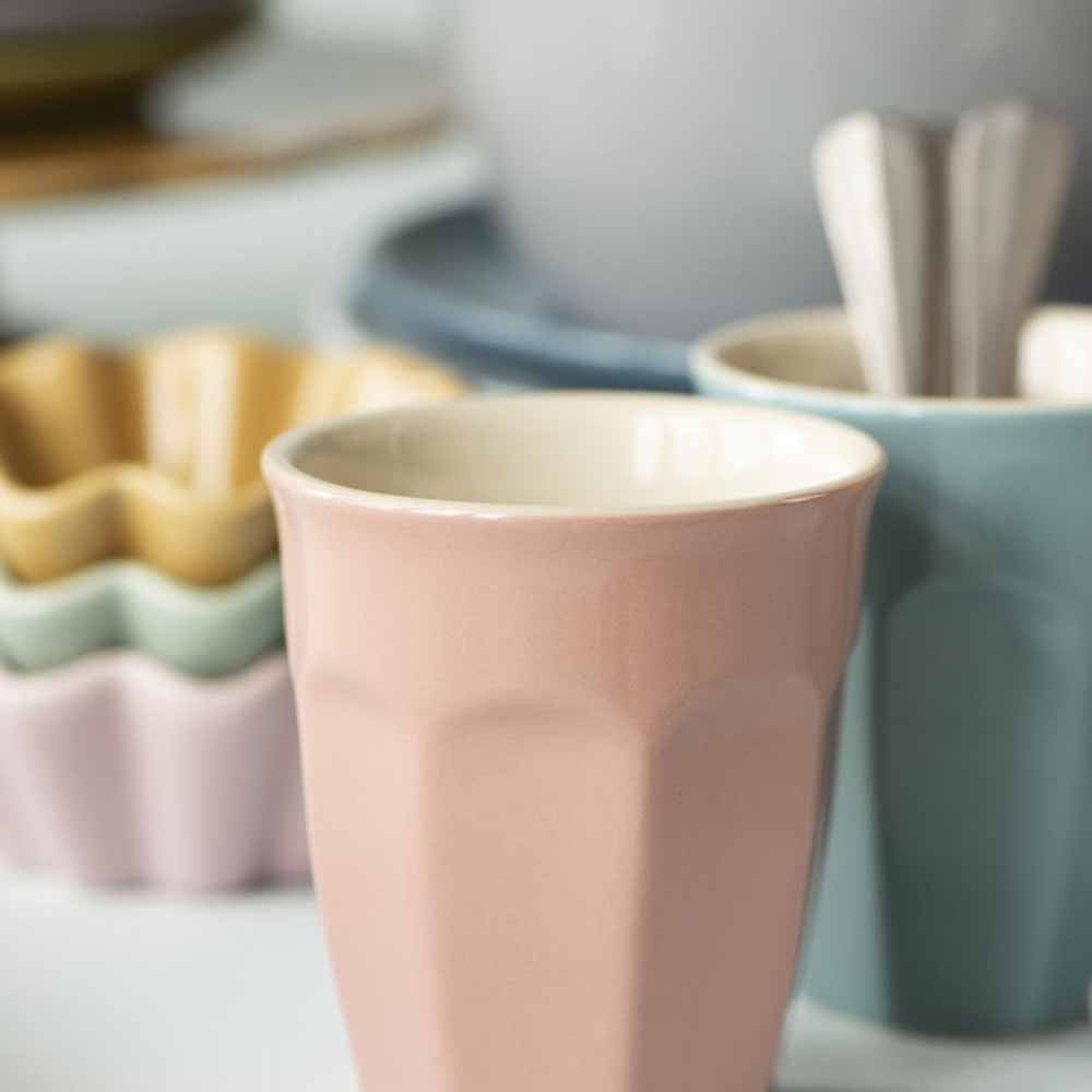 Nahaufnahme eines Ib Laursen - Cafe Latte Bechers Mynte im Vordergrund mit verschiedenen pastellfarbenen Küchenutensilien, die im Hintergrund leicht verschwommen sind.