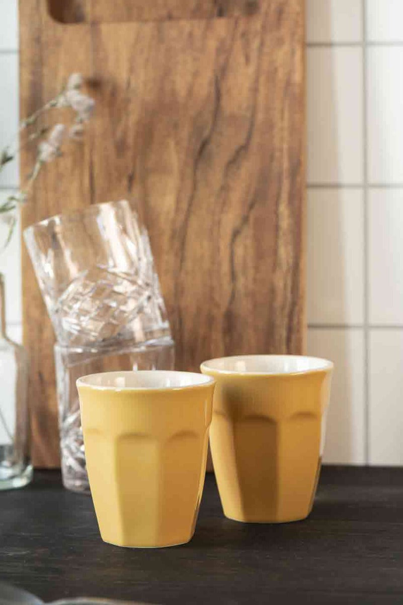 Zwei Ib Laursen - Cafe Latte Becher Mynte auf einer dunklen Holzarbeitsplatte mit einem Glas und einem Holzbrett im Hintergrund.
