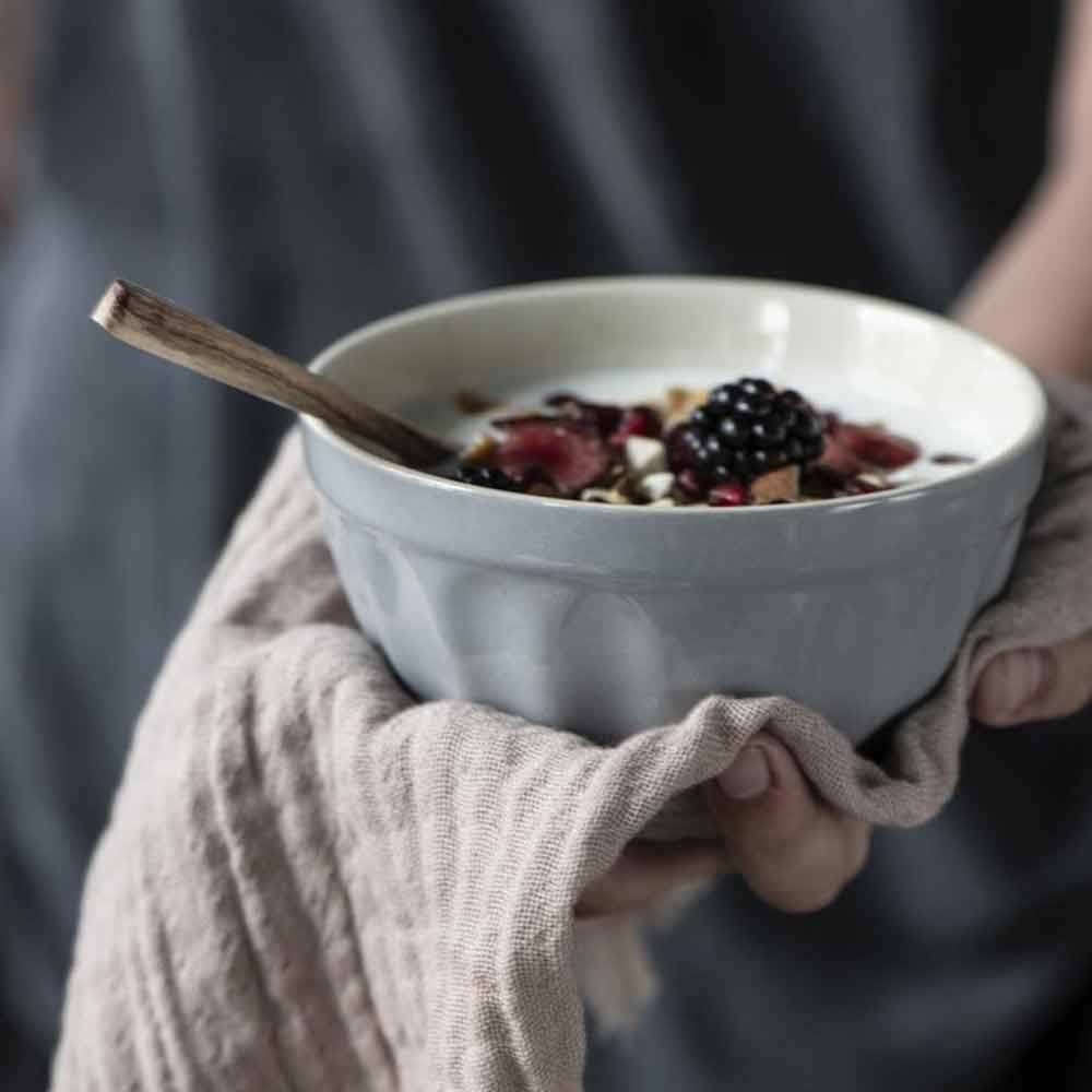Person hält eine Müslischale Mynte mit Beeren und Granola, mit sichtbarer Zimtstange, in einer kuscheligen Strickhülle.