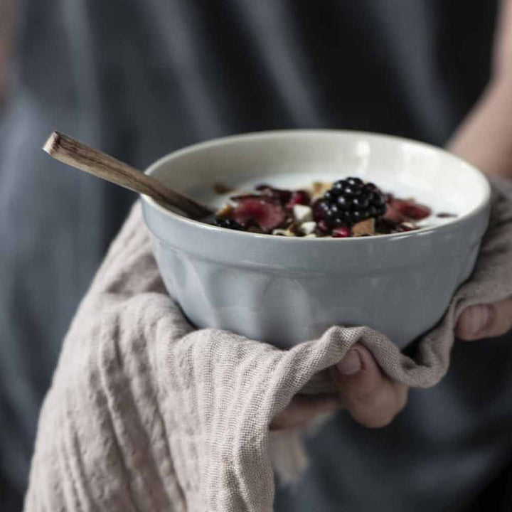 Person hält eine Müslischale Mynte mit Beeren und Granola, mit sichtbarer Zimtstange, in einer kuscheligen Strickhülle.