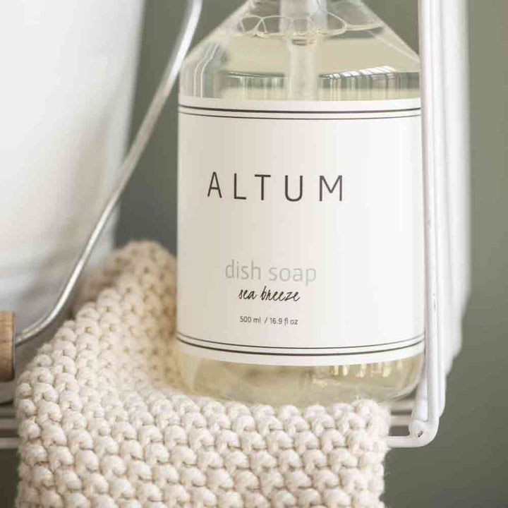 Nahaufnahme einer Flasche mit der Aufschrift „Ib Laursen – Topflappen Mynte Spülmittel“ mit einer klaren Flüssigkeit darin, neben einem weißen gewebten Tuch platziert.