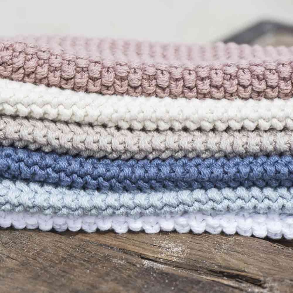 Ein Stapel ordentlich gefalteter Ib Laursen - Topflappen Mynte in den Farben Rosa, Blau und Creme, platziert auf einer rustikalen Holzoberfläche.