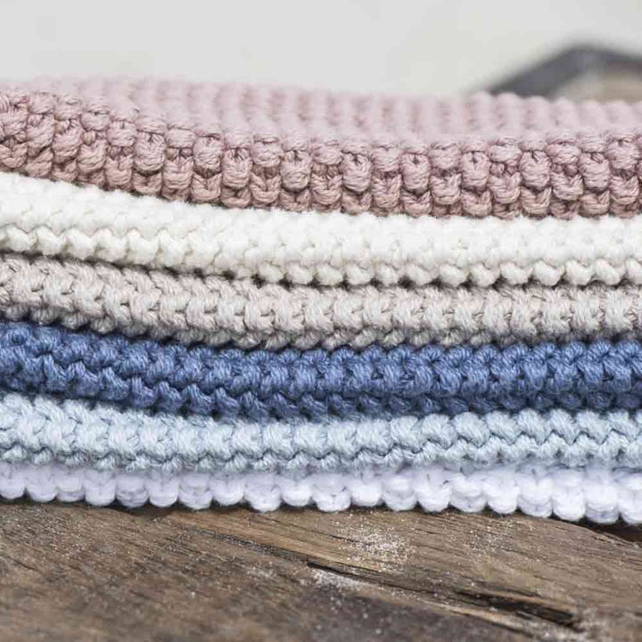 Ein Stapel ordentlich gefalteter Ib Laursen - Topflappen Mynte in den Farben Rosa, Blau und Creme, platziert auf einer rustikalen Holzoberfläche.