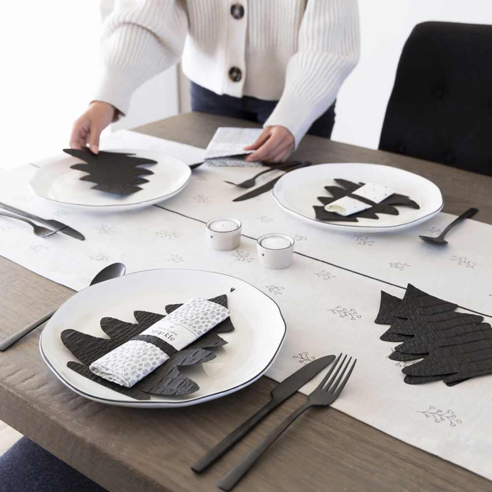 Eine Frau deckt einen Tisch mit Bastion Collections – Serviettenhalter Weihnachten Tanne 6er Set Tellern und Servietten.