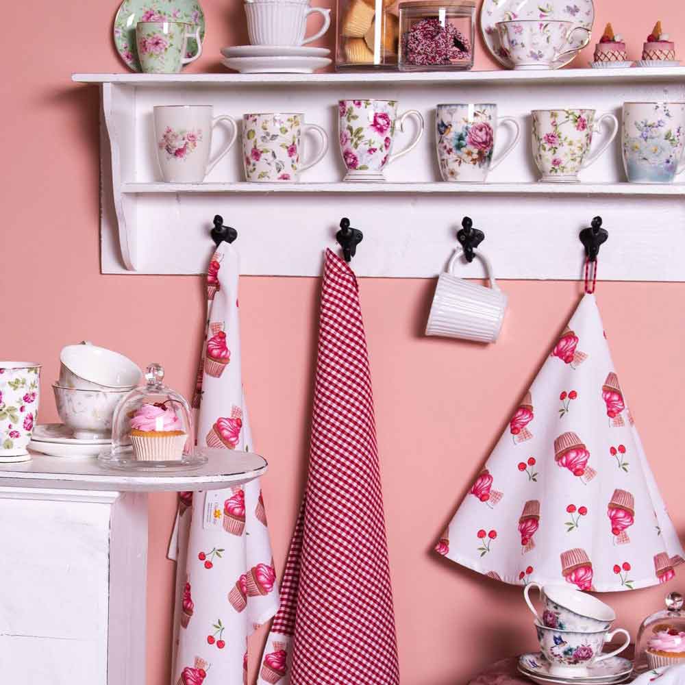 Eine Küchenecke im Vintage-Stil mit Clayre & Eef – Geschirrtuch Cupcake Cherry rund auf einem Regal und verschiedenen Schürzen, die darunter hängen.
