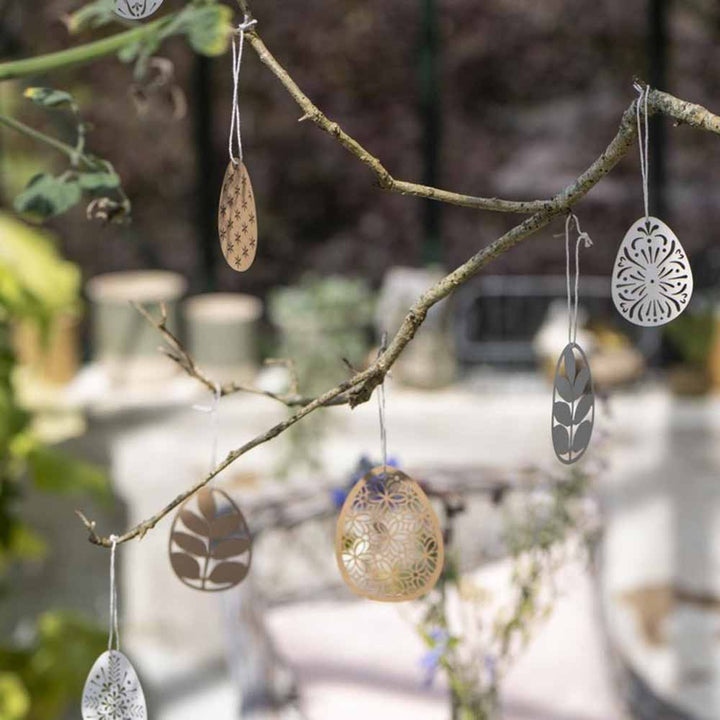 Dekorative Eier von Ib Laursen – Scherenschnitt Ei Blumenmuster, die an einem Ast in einer Gartenumgebung hängen.