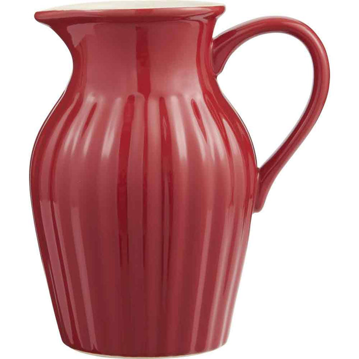 Ein glänzend roter Ib Laursen - Krug Mynte 1,7 Liter Krug mit geschwungenem Henkel und senkrechten Rillen, isoliert auf weißem Hintergrund.