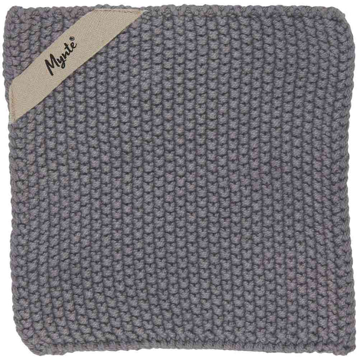 Ein quadratisches, handgestricktes, graues Geschirrtuch mit einem kleinen beigen Etikett mit der Aufschrift „Ib Laursen – Topflappen Mynte“ in der oberen linken Ecke.