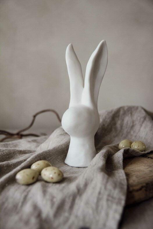 Eine große Figur von Majas Cottage – Hase, umgeben von gesprenkelten Eiern auf einem drapierten Tuch.