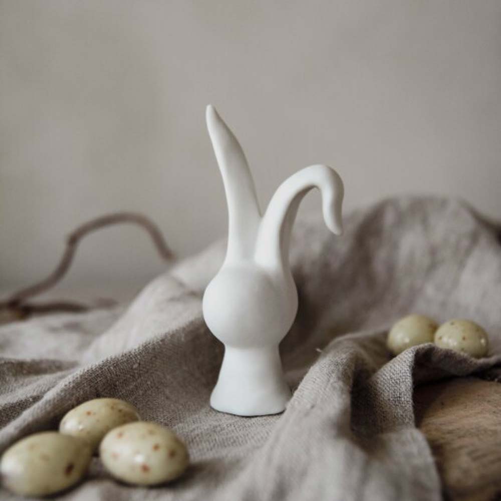 Eine kleine Majas Cottage – Hase-Figur, umgeben von gesprenkelten Eiern auf einem drapierten Tuch.