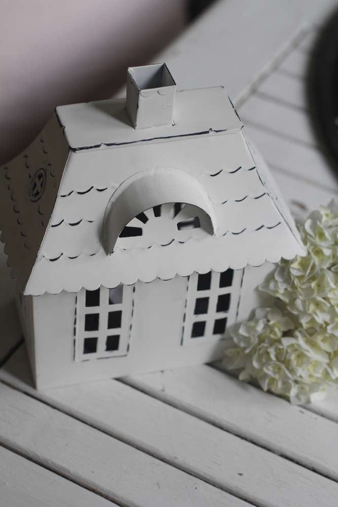 Ein VL Home – Metallhaus weiß mit Walmdach klein auf einem Holztisch.
